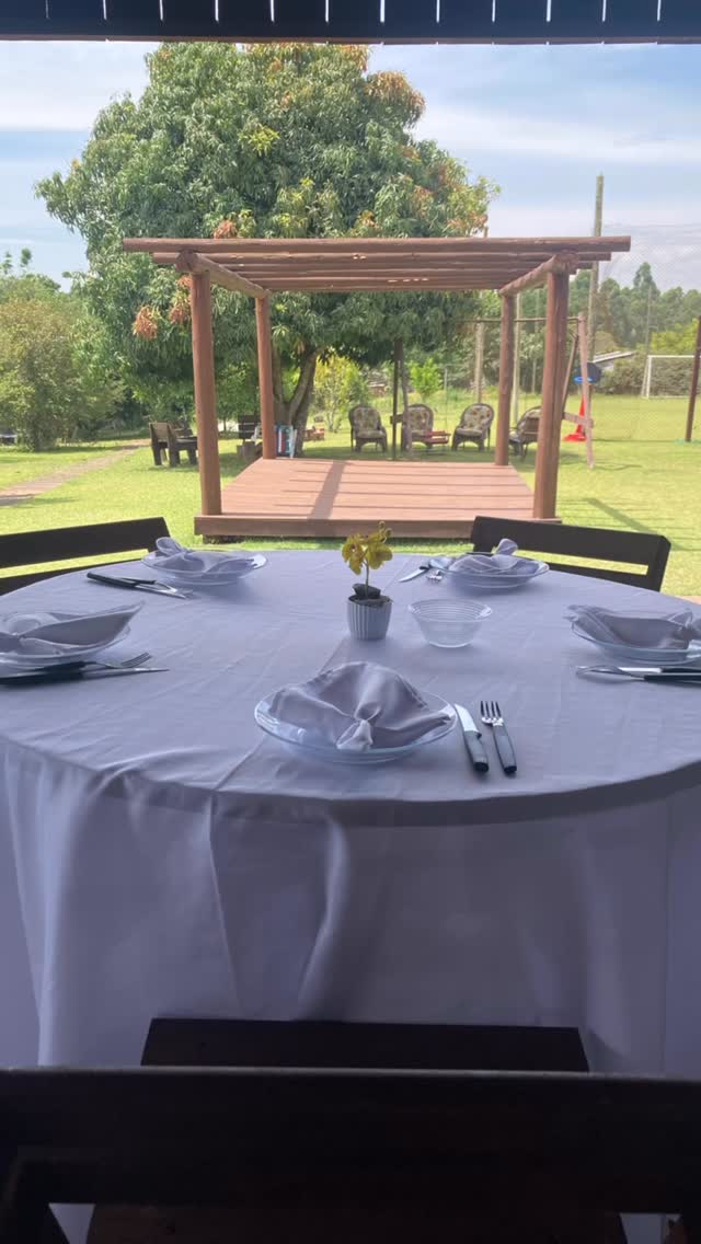 Mesa posta com toalha branca diante da pérgola